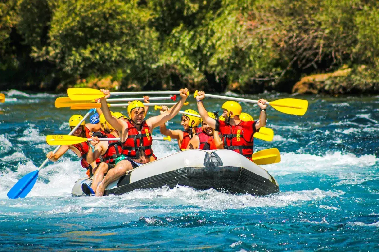 Grupo de viajeros celebrando con los remos en alto durante un descenso de rafting